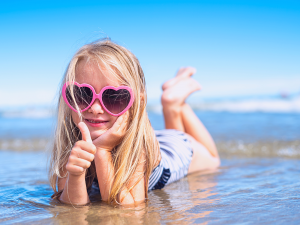 Tyttö loikoilee rannalla aurinkolasit päässä ja näyttää peukkua