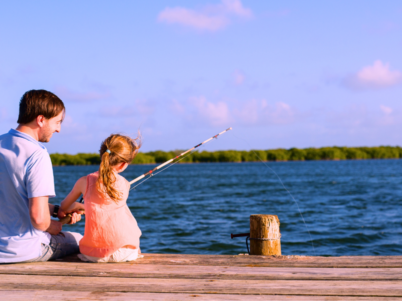 Isä ja kouluikäinen tytär kalastavat kesäpäivänä laiturilla.