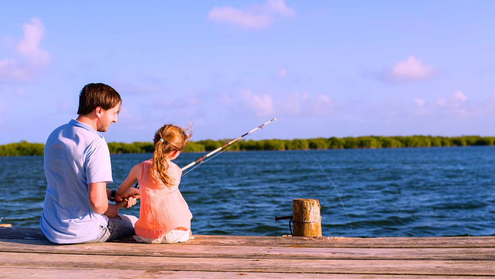 Isä ja kouluikäinen tytär kalastavat kesäpäivänä laiturilla.