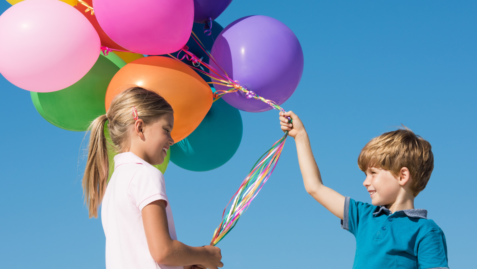 Lapset pitävät kiinni ilmapalloista nauraen. Taustalla sininen taivas.