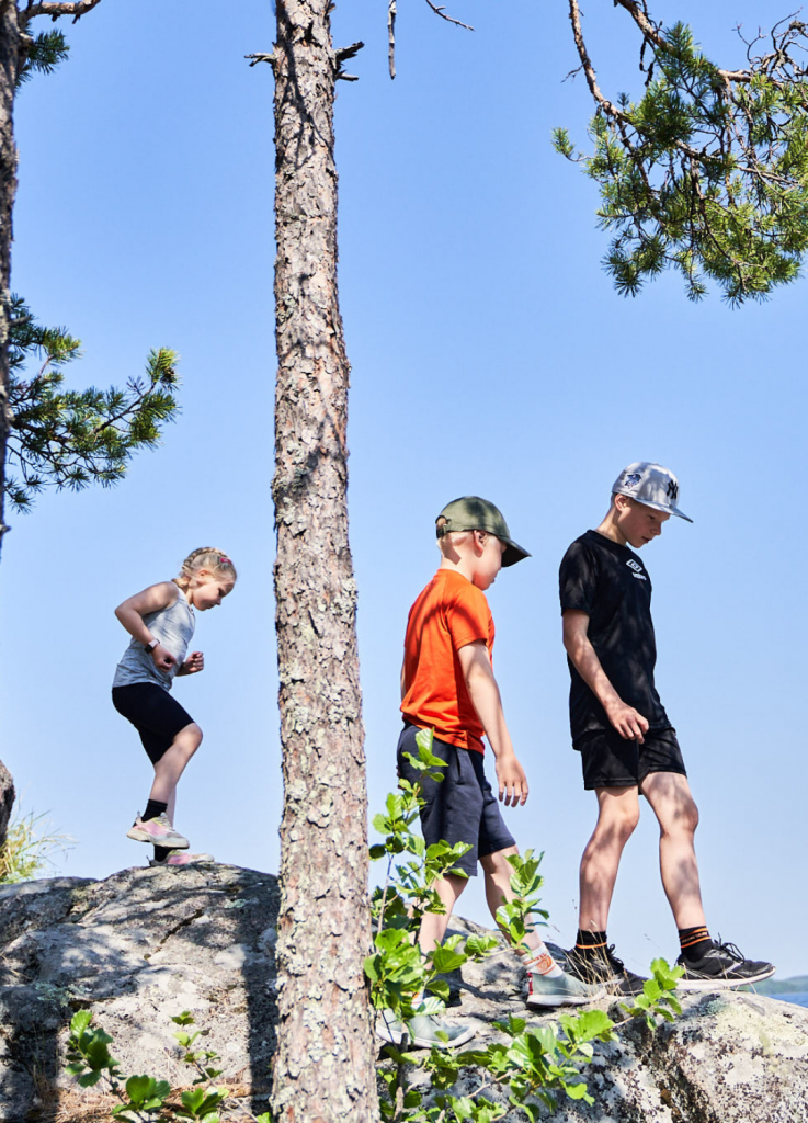 Kolme kouluikäistä lasta kävelee kallioilla kesäisessä säässä.